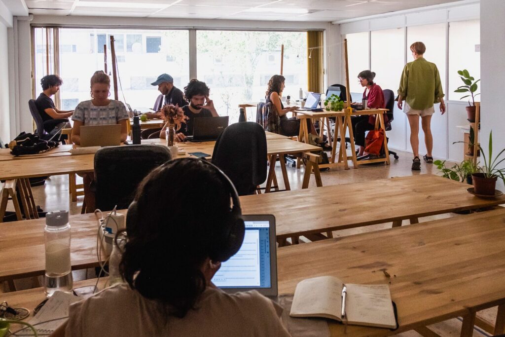 Picture from the Cowork showing wooden tables and people working at them on their laptops.